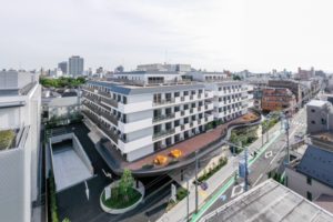 施設全体の高所からの俯瞰写真。複数階建ての白基調の建物と周辺市街地が見える。